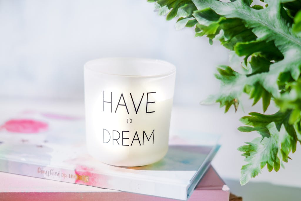 A motivational candle with 'Have a Dream' text, resting on books with greenery around.